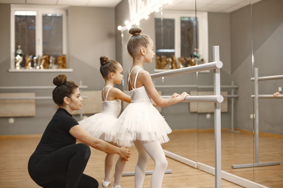 Young ballerinas learning ballet at the barre with a teacher in a dance studio.