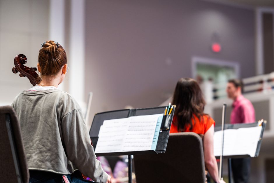 Cellist and musicians rehearsing in a symphony orchestra setting indoors.